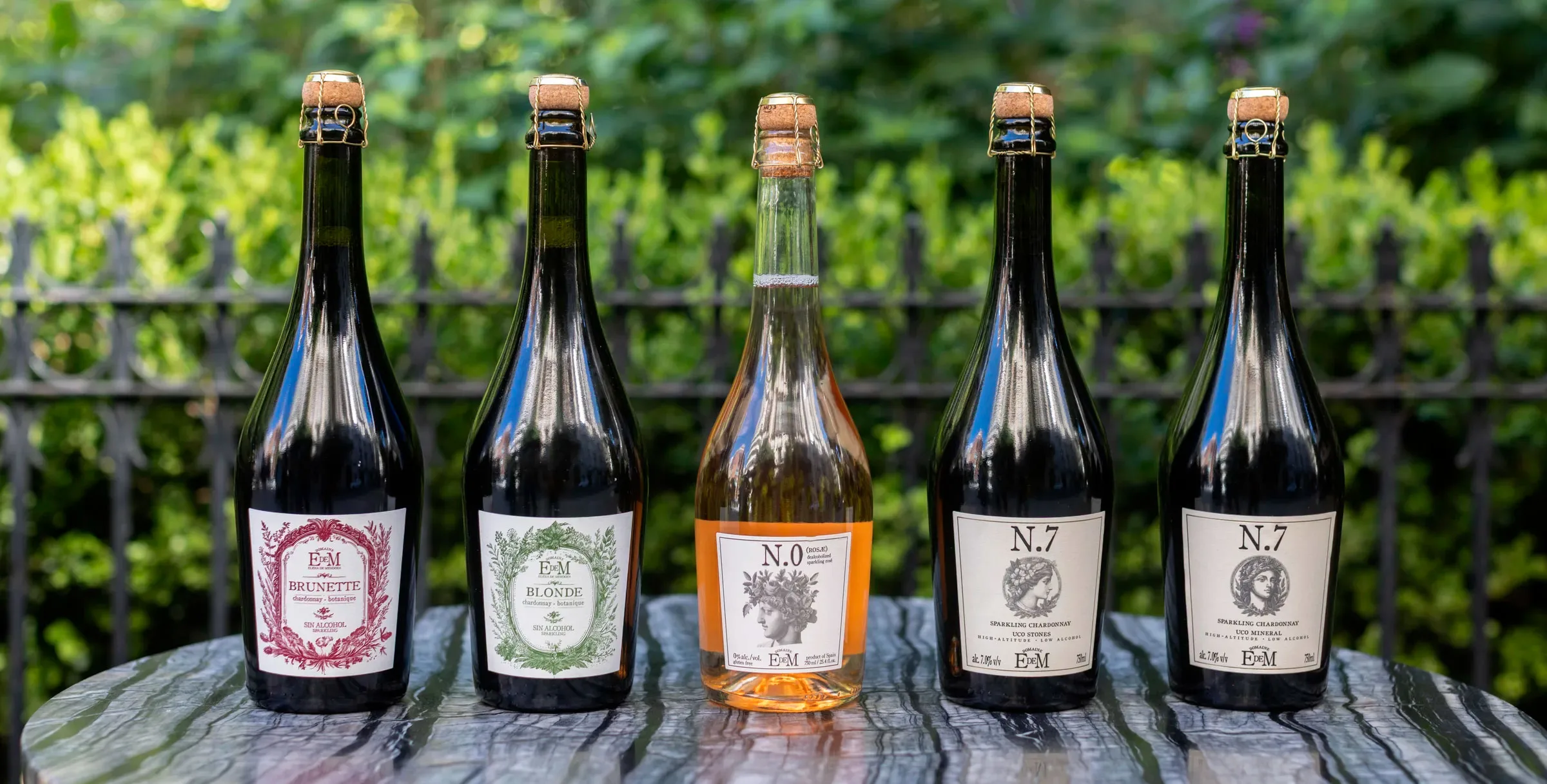 The five Domaine EdeM sparkling wines lined up on a table in front of the vineyard