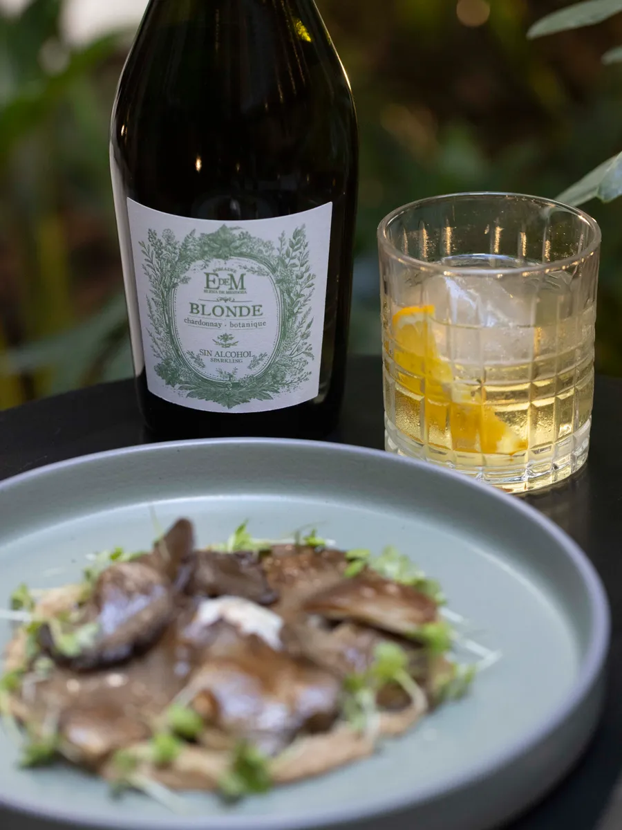 Bottle of BLONDE with a tumbler and a plate of food among plants