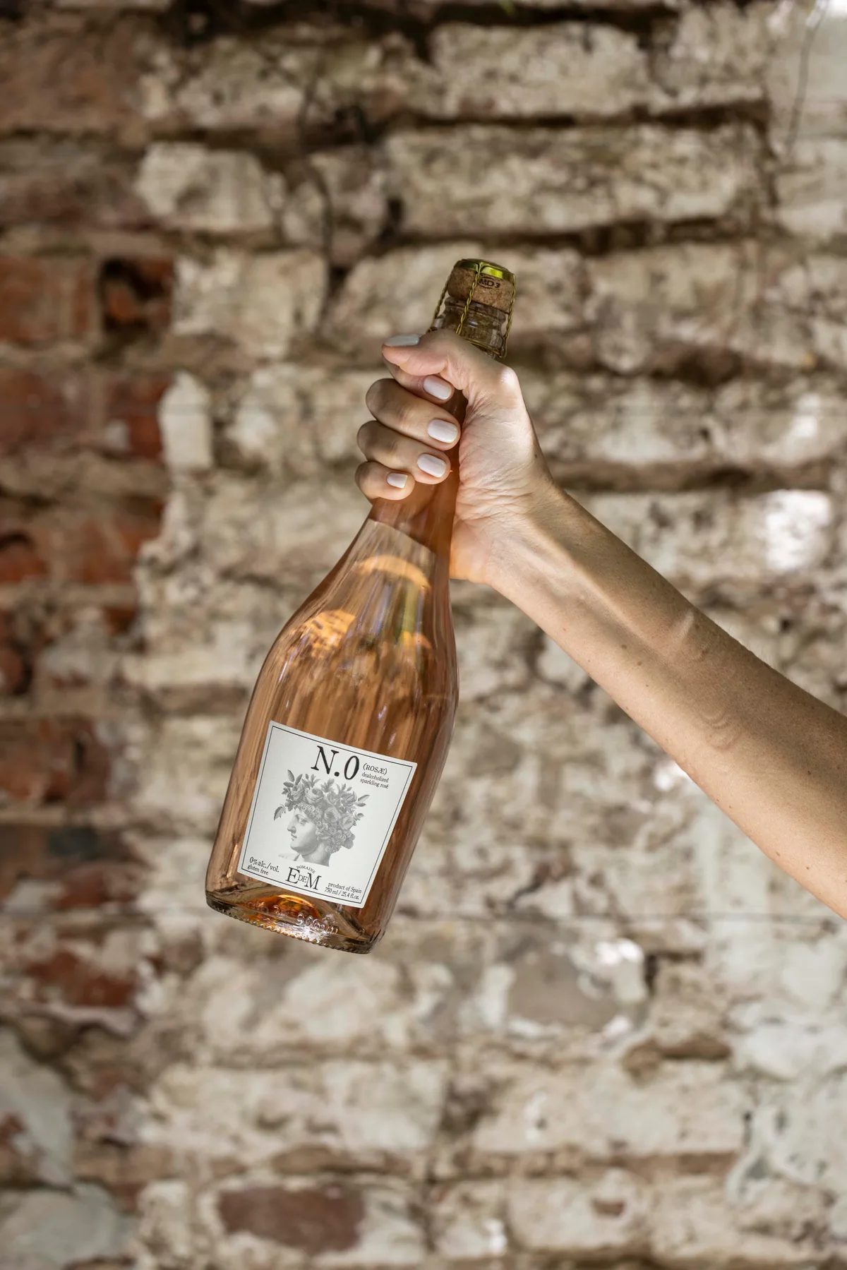 A hand holding a bottle of ROSAE against a brick wall